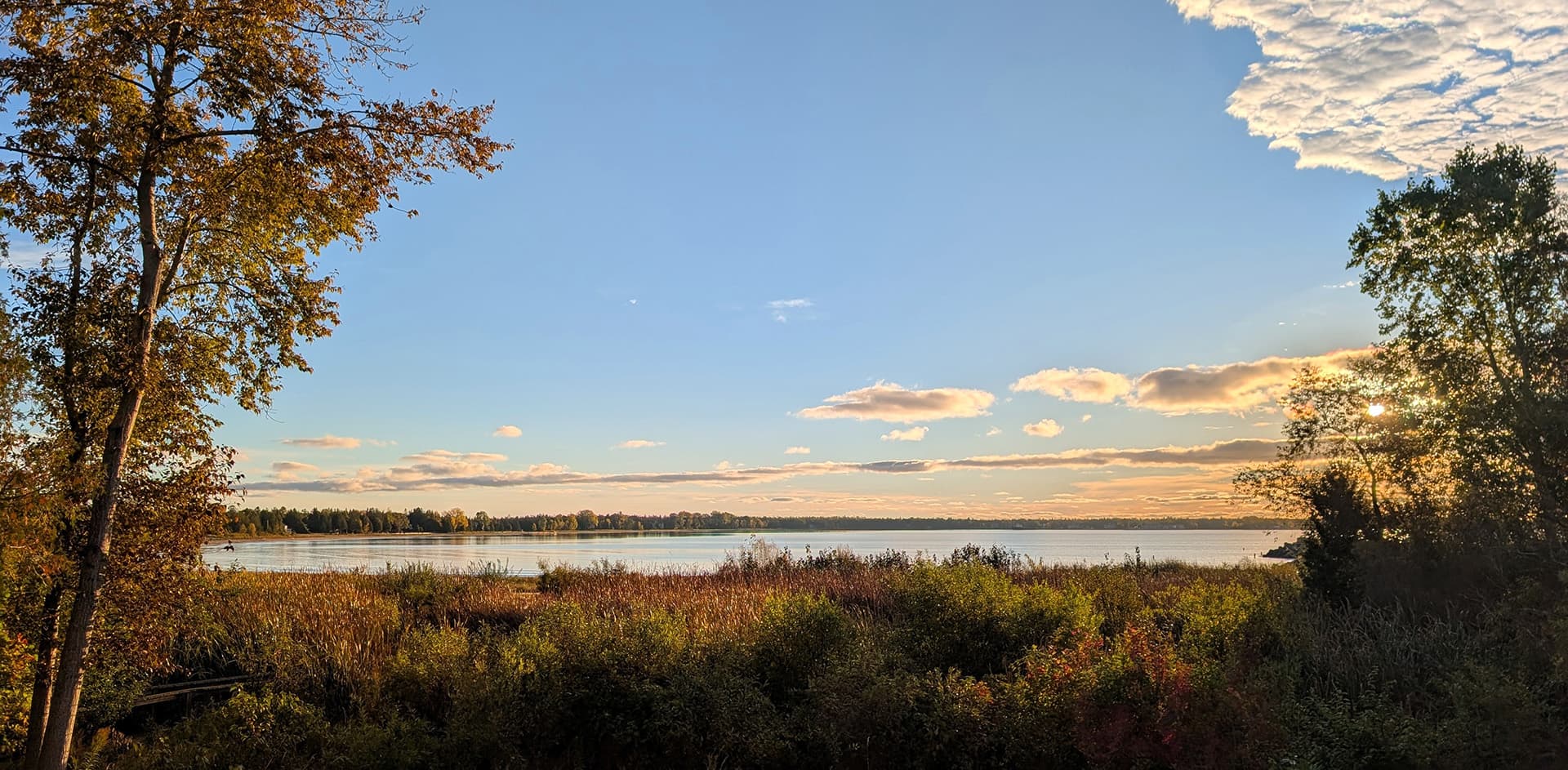 A serene lake view surrounded by trees with colorful clouds at sunset.