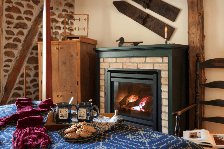 A cozy room featuring a fireplace, a wooden cabinet, mugs, cookies, and a warm blanket.