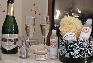 A cozy setting featuring champagne, two glasses, and spa products beside a fireplace.