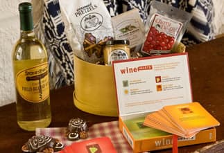 A wooden basket containing a bottle of wine, snacks, and a boxed game about wine pairings.