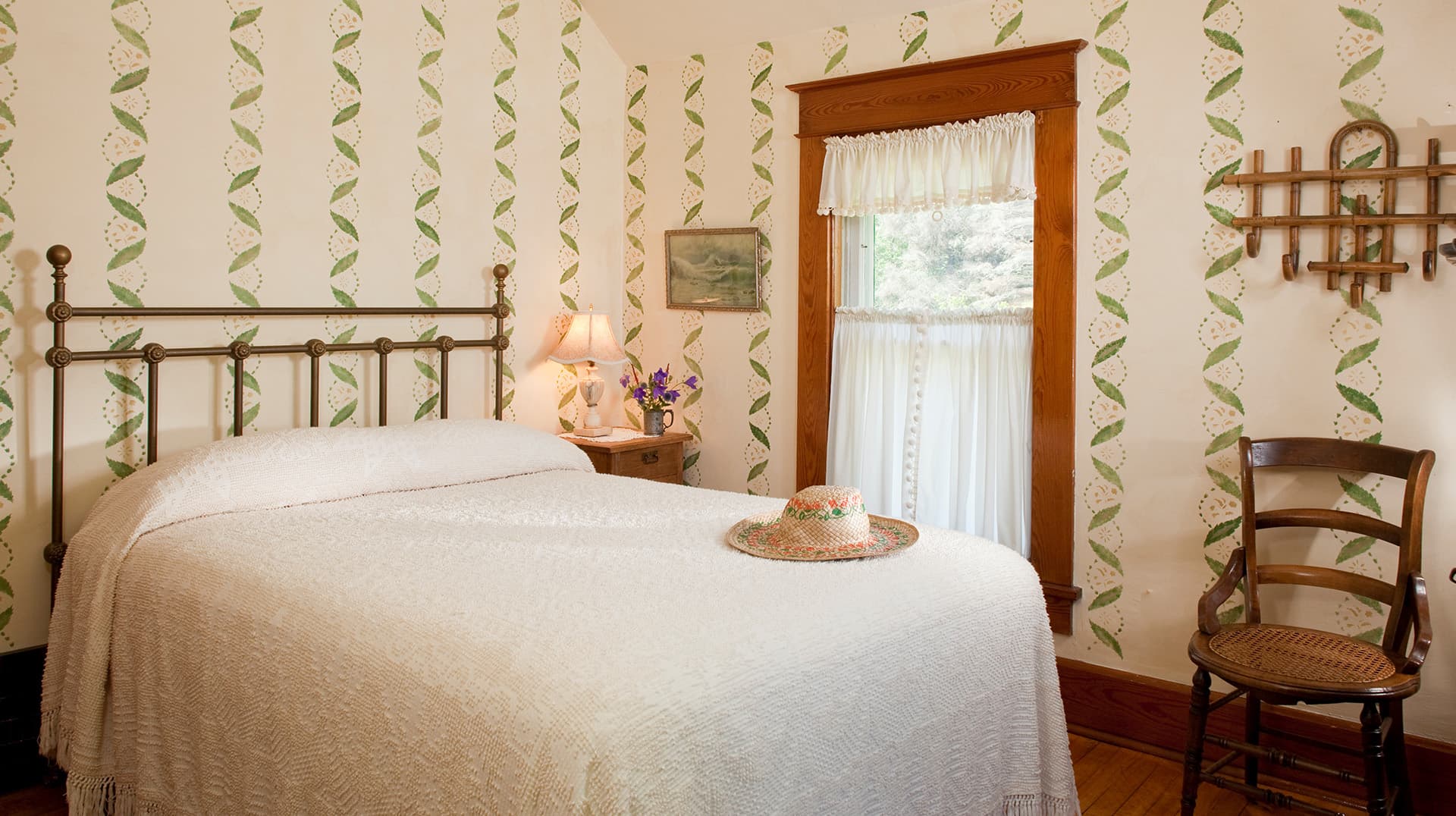 A cozy bedroom featuring a wrought-iron bed, floral wallpaper, and a wooden chair.
