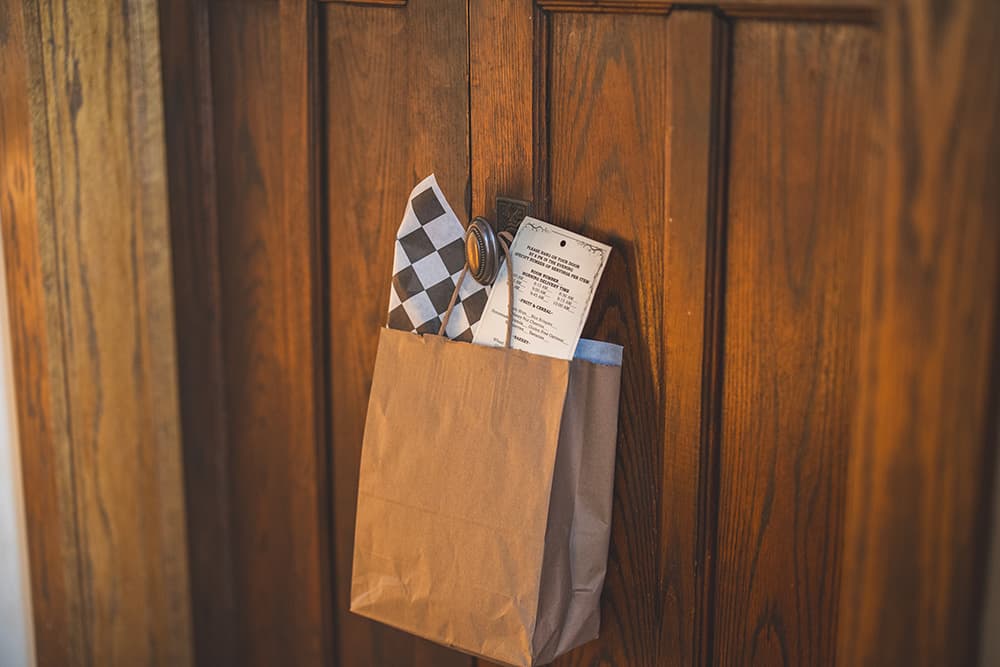 A paper bag containing items is hung on a wooden door.